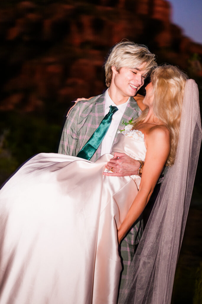 Groom holding bride in arm in her blush pink wedding dress, with bright flash, movement blur, cathedral rock in the background in Sedona AZ