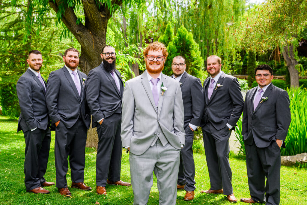 groom forward to camera and groomsmen behind on green lawn with trees at the Windmill House Chino Valley Arizona
