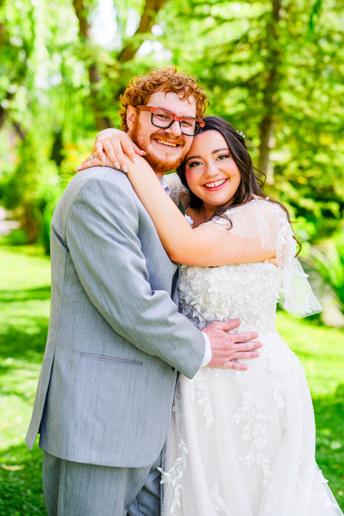bride and groom hugging each other and smiling at camera with green trees background at the Windmill House Chino Valley Prescott Arizona