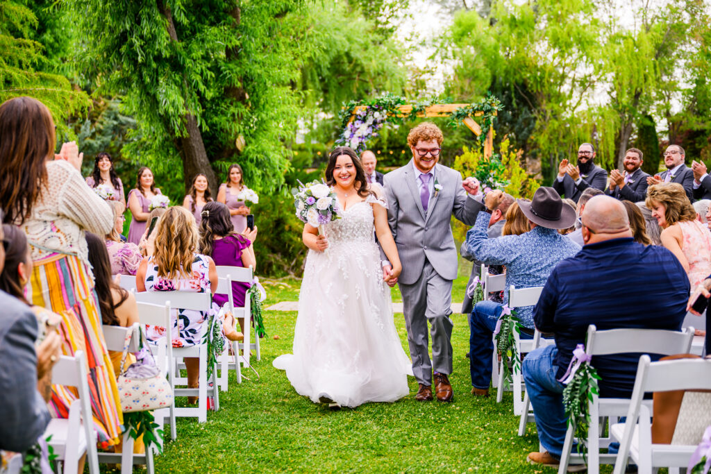 bride and groom walking down aisle as guests watching on lawn with trees in the background at the Windmill House Chino Valley Arizona 