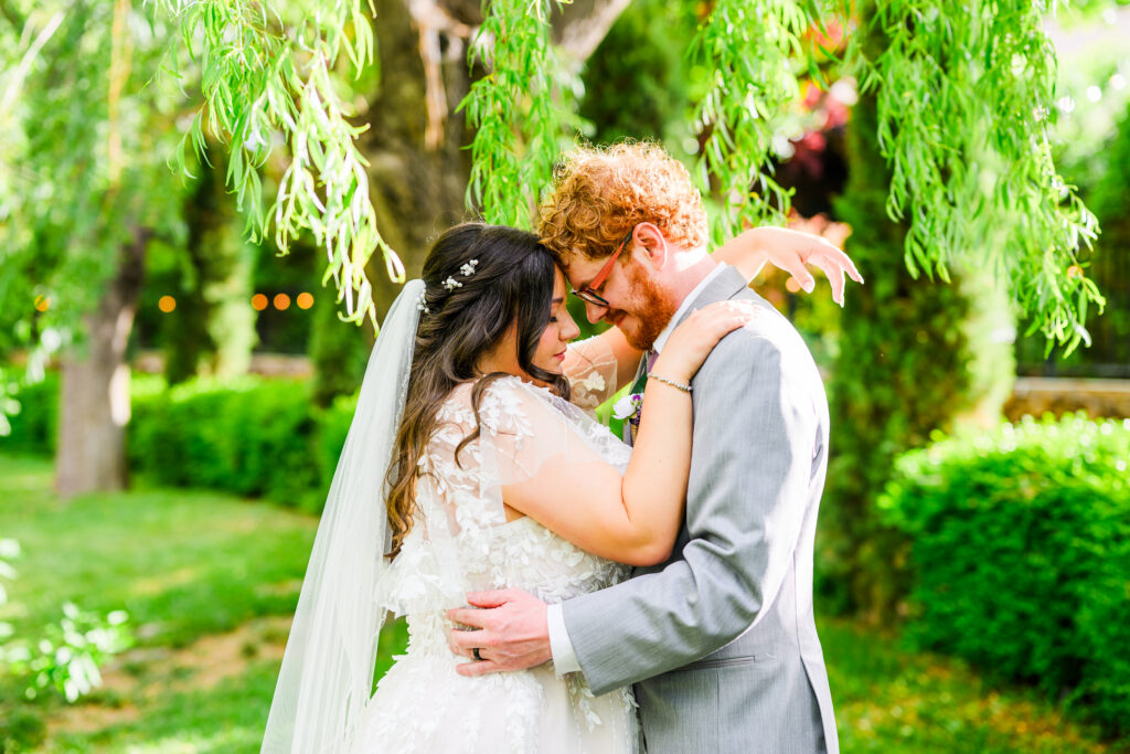bride and groom touching foreheads with closed eyes under willow tree and green background at the Windmill House Prescott Chino Valley Arizona