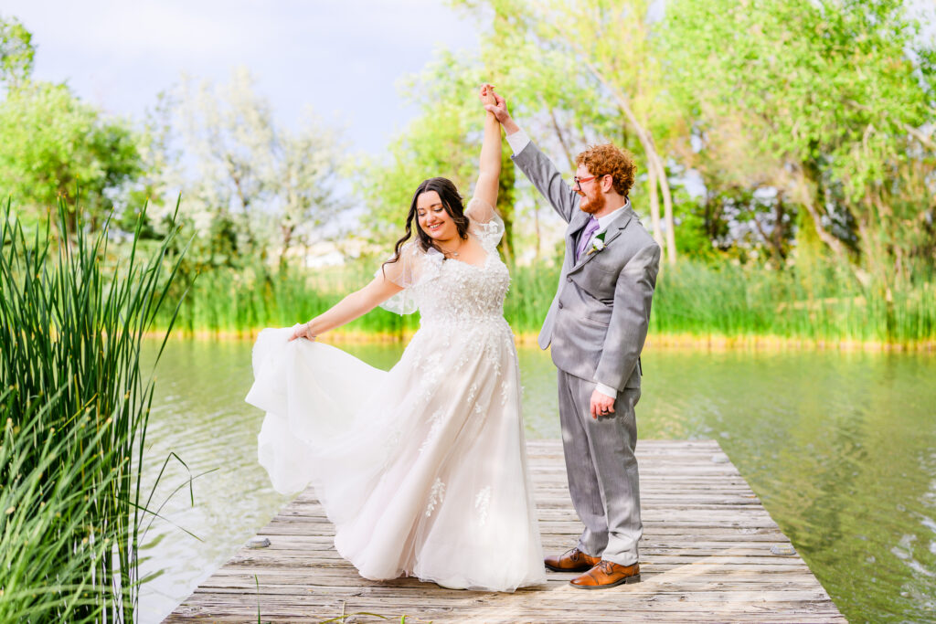 Bride and groom dancing on dock, groom twirling bride with forest and lake background at the Windmill House in Chino valley Prescott Arizona