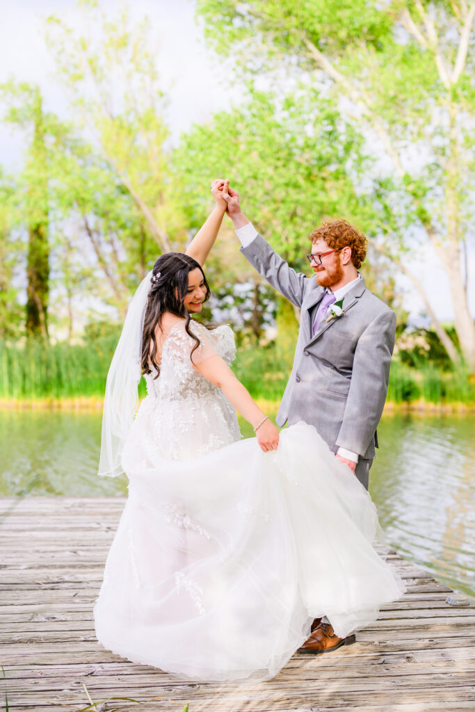 Bride and groom dancing on dock, groom twirling bride with forest and lake background at the Windmill House in Chino valley Prescott Arizona