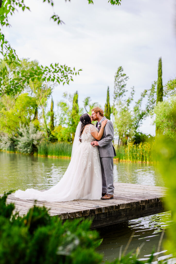 Bride and groom kissing dock, with forest green and lake background at the Windmill House in Chino valley Prescott Arizona